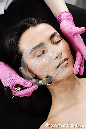 Process of face massage with black stone roller close-up. Cosmetologist using stone roller for face massage for girl Stock Photo