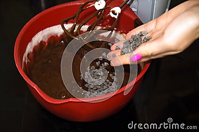 The process of making chocolate brownie cake. the girl adds with the palm of a new batch of chocolate for whipping with a mixer Stock Photo