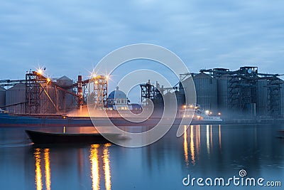 The process ofLoading cargo barges at the river port at night on a long shutter speed. The illuminated urban landscape Stock Photo