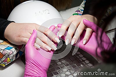 process of performing manicure in beauty salon. Manicurist in pink gloves holding and examining hands of client. Professional hand Stock Photo