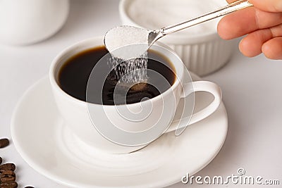 The process of pouring white sugar from a spoon into a white cup of coffee. Sugar addict, diabetes. Stock Photo