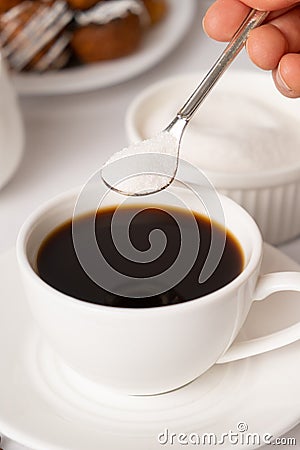 The process of pouring white sugar from a spoon into a white cup of coffee. Sugar addict, diabetes. Stock Photo