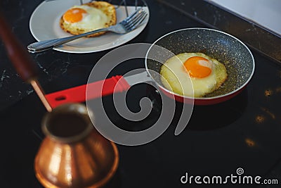 Process of preparing a classic breakfast: fried eggs in a frying pan, a classic Turkish Turk for cooking coffee on a glass hob. Stock Photo