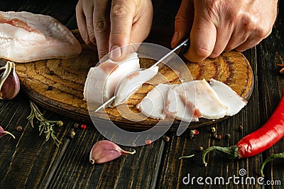 The process of preparing sandwiches for a snack from lard and garlic in the kitchen. Chef hands use a knife to cut pork lard on a Stock Photo