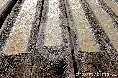 Process of production and crystallization of salt from sea water. Gutters hollowed into palm trunks. The sun evaporates sea water Stock Photo