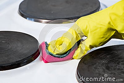 The process of washing an electric stove. A hand in a yellow glove cleans the white surface of dirt. Homework cleaning Stock Photo