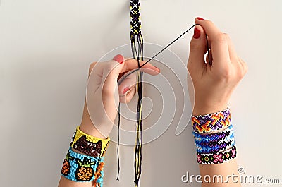 Process of weaving knot for DIY friendship bracelet. Female hands with many handmade bracelets on wrists. step by step. Stock Photo