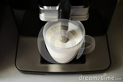 The process of whipping milk with steam. A cup of milk and a coffee machine for whipping. Spout in a cup. Stock Photo