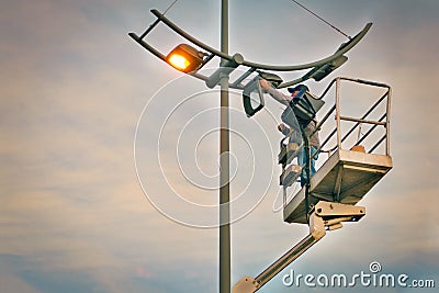 Profession repair and maintenance of street lamps - crane lifted an electrician to replace bulbs at sunset in evening. Stock Photo