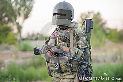 Professional airsoft player stands in a big helmet and a machine gun. Stock Photo