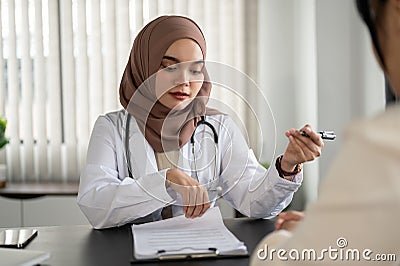 A professional Asian Muslim female doctor diagnoses a patient's symptoms in an examination room Stock Photo