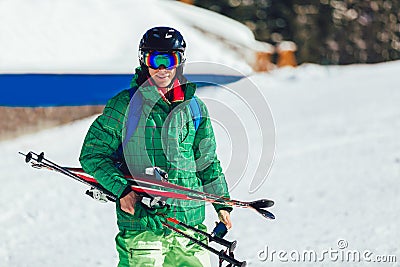 Professional athlete skier in an green jacket wearing a black mask and holding skis Stock Photo