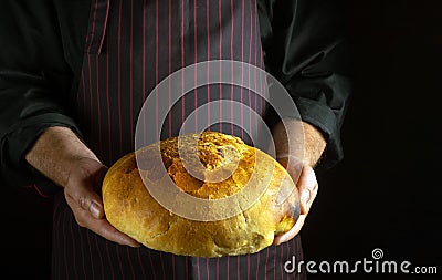 Professional baker holds fresh wheat bread in his hands. The concept of baking bread in the bakery. Place for prescription on dark Stock Photo