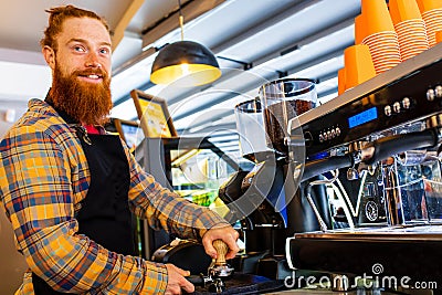 Professional barista young redhaired ginger bearded man in black apron working in coffee shop Stock Photo