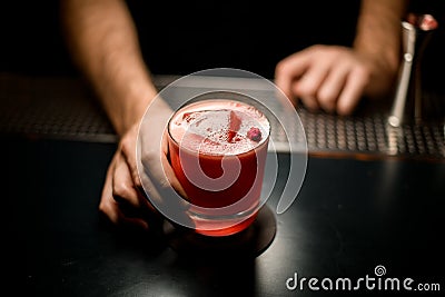 Professional bartender serving the red color alcoholic cocktail drink decorated with a little rose bud Stock Photo