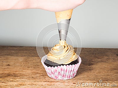 Professional cake baker applying frosting on a chocolate cupcake Stock Photo