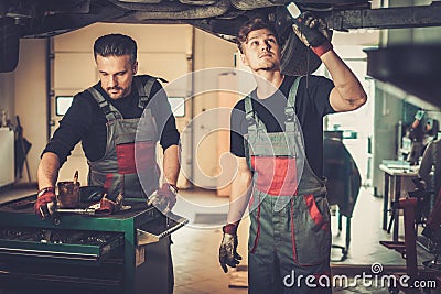 Professional car mechanics working under lifted car in auto repair service. Stock Photo