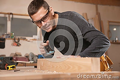 Professional carpenter grinding plank with jack plane in workshop Stock Photo