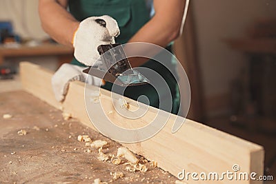 Professional carpenter grinding wooden plank with jack plane in workshop Stock Photo