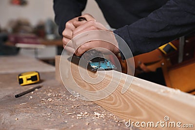 Professional carpenter grinding wooden plank with jack plane in workshop Stock Photo
