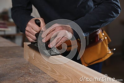 Professional carpenter grinding wooden plank with jack plane in workshop Stock Photo