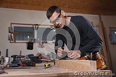 Professional carpenter grinding plank with jack plane in workshop Stock Photo