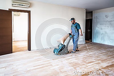Professional carpenter worker grinding sanding wooden parquet floor by using floor sander Stock Photo
