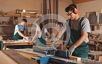 Professional carpenter working with surface planer and colleagues Stock Photo