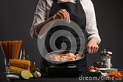 Professional chef fries and salts the shrimp on a background of vegetables. Seafood and wholesome food Stock Photo