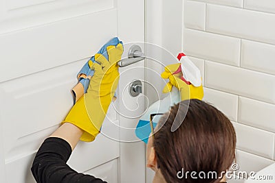 Professional cleaning services. Woman worker in rubber gloves doing cleaning in the bathroom, cleaning door with rag and detergent Stock Photo