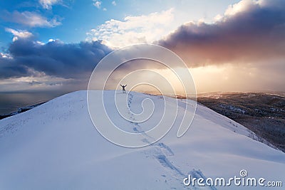 Professional climber on the snowshoeing at the top of the rock with his hands up is pleased with the next victory of the ascent an Stock Photo