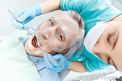 Professional dentist curing scared mature patient in dental clinic Stock Photo