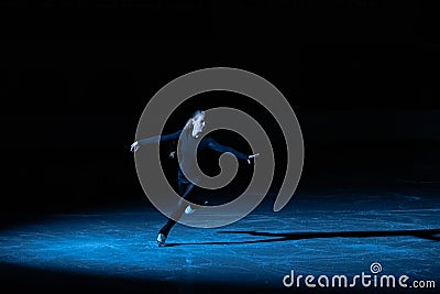 Professional figure skating artist slides and spins on the ice in the arena in the rays of blue light. Young woman Stock Photo