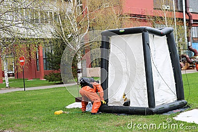 A professional firefighter in an orange special fireproof suit prepares to assemble a white oxygen tent to rescue people at a chem Editorial Stock Photo
