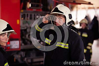 Professional firefighters with uniforms and protective helmets getting ready for action. Firetruck in the background Stock Photo