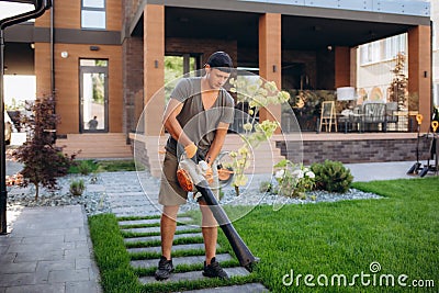 Professional Gardener with Leaf Blower in His Hand Cleaning Residential Backyard Garden. Gardening and Landscaping Stock Photo