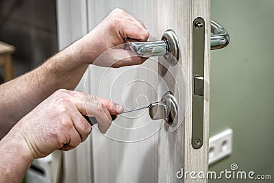 Professional handyman repair the door lock in the room, locksmith fixing lock with screwdriver Stock Photo