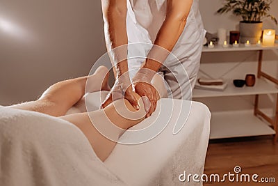 Professional legs massage in SPA salon on the background of candles. Handsome masseur therapist in white uniform making Stock Photo
