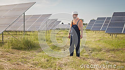 Professional man technician in hard hat walks on new ecological solar construction outdoors. Farm of solar panels Stock Photo