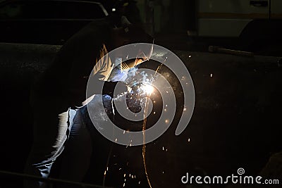 Professional mask protected welder man working on metal welding and sparks of metal at night. Employee welding steel with sparks Stock Photo