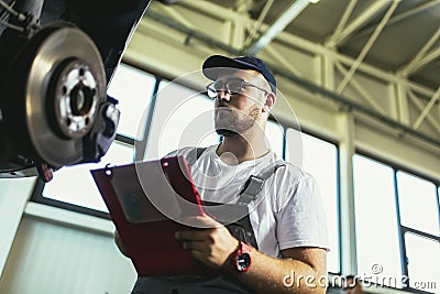 Professional near the car hanging on the lift at the service station make a diagnostics, repair the brakes Stock Photo