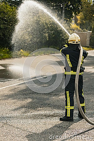 One young male firefighter on duty dressed in uniform with water hose sprinkling water Stock Photo