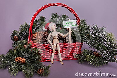 Merry Christmas picket sign jointed doll wearing Santa hat winter scene red basket and pine cones Stock Photo