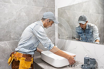 Professional plumber, male worker in uniform installing sink and water pipe in new apartment Stock Photo