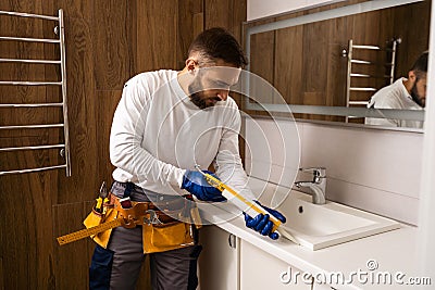 Professional plumber, male worker in uniform installing sink and water pipe in new apartment Stock Photo