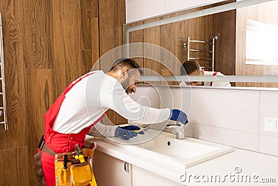 Professional plumber, male worker in uniform installing sink and water pipe in new apartment Stock Photo