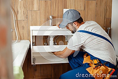 Professional plumber, male worker in uniform installing sink and water pipe in new apartment Stock Photo