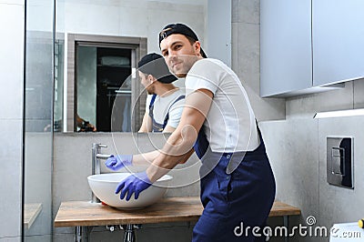 Professional plumber, male worker in uniform installing sink and water pipe in new apartment. Stock Photo