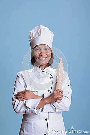 Professional positive asian cook standing with arm crossed holding kitchen rolling pin Stock Photo