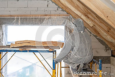 Professional roofer man installing thermal insulation layer with fiberglass wool under the roof Stock Photo